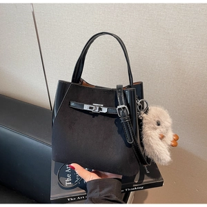 Dettaglio borsa a secchiello nera con fibbia argento e ciondolo peluche sopra dei libri