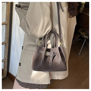 Detail of dark brown bucket bag with white stitching and decorative metal buckle strap