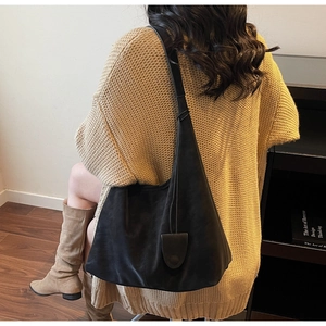 Detail view of a large black leather hobo tote bag worn with casual autumn knitwear