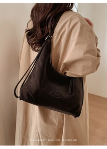 Detail einer großen kaffeebraunen Wildleder-Tragetasche mit Logo auf einem weiblichen Model