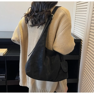 Detail of a large black leather hobo bag with adjustable strap worn on a beige sweater