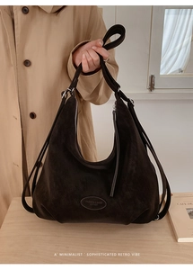 Detail einer schwarzen Hobo-Tasche aus Wildleder mit ovalem Lederlogo und Riemen