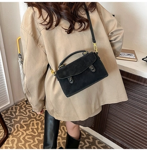 Detail of matte black crossbody bag with curved flap and gold-tone hardware shown on model
