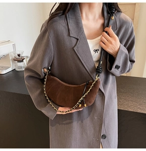 Brown suede croissant bag worn by a model in a cafe setting with a chain strap