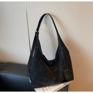 Detail view of large matte black leather tote bag with square charm on dark sofa
