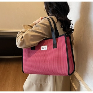 Détail du sac cabas à carreaux rouges avec anses noires porté sur un trench-coat kaki