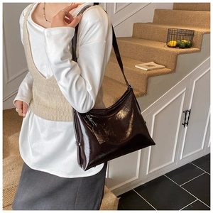 Detail view of large dark brown patent leather shoulder bag with metallic stud accents