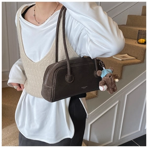 Détail du sac à bandoulière en daim marron foncé avec surpiqûres et breloque ours