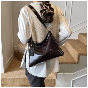Detail of a large dark brown hobo bag in glossy patent leather shown on a model