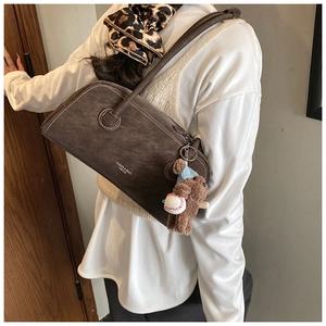 Gros plan du sac bandoulière en daim marron avec surpiqûres blanches et charm ours