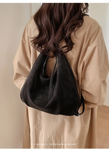 Detail der schwarzen matten Wildledertasche mit ovalem Lederlogo und Metallreißverschluss