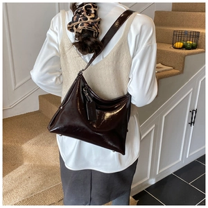 Detail of a deep brown glossy leather bucket bag worn over the shoulder in a cozy setting