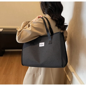 Vue de profil du sac cabas à carreaux avec écusson blanc sur trench-coat camel