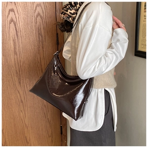 Detail of glossy deep brown shoulder bag with metallic hardware and decorative tag