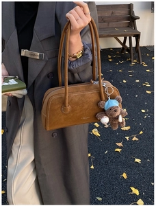 Détail du sac Boston en daim caramel avec un charm ours dans un parc d'automne pittoresque