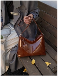 Detail of deep brown patent leather bucket bag with glossy crinkle texture and slim strap