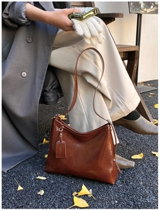 Close-up of dark brown oily leather bucket bag with brand tag on autumn ginkgo leaves