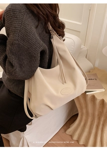 Detail of minimalist leather tote bag featuring a leather logo patch and zip closure