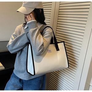 Détail d'un grand sac cabas en toile blanche avec bordure noire porté à l'épaule
