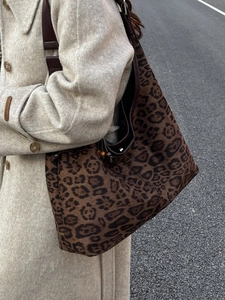 Large leopard print tote bag with brown leather strap worn over a beige coat