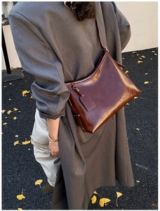 Detail view of deep brown glossy leather shoulder bag with sleek rectangular tag and logo