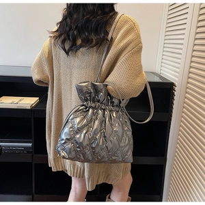 Detail view of silver quilted drawstring bucket bag styled with a beige knit sweater