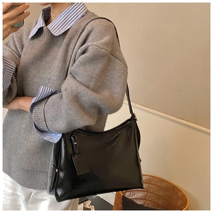 Detail of black glossy pleated shoulder bag with adjustable strap on model for daily use