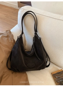 Detail einer großen schwarzen Hobo-Tasche aus Wildleder mit Logoprägung auf dem Sofa