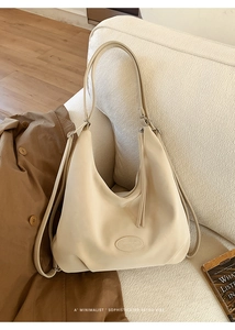 Detail einer cremeweißen Leder-Tote-Bag mit seitlichen Quasten und Logoprägung auf Sofa