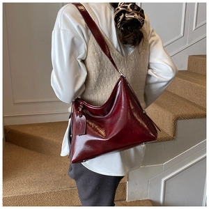 Model wearing dark burgundy large bucket bag made of glossy leather with shoulder strap