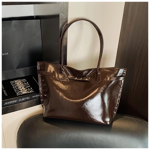 Detail of a brown glossy tote bag with silver rivets and minimalist shoulder straps