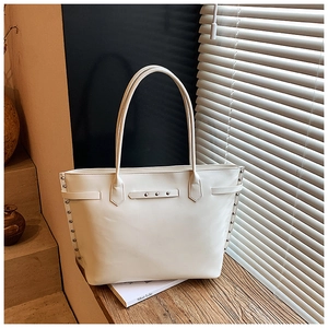 Close-up of white tote bag with metal rivets on a wooden table under natural light