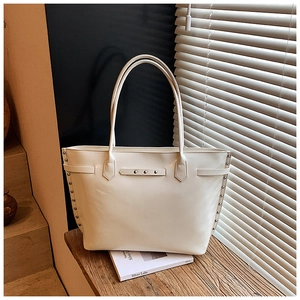 Detail of cream white leather tote bag featuring decorative silver studs on a wooden bench