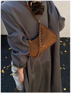 Detalle de bolso hobo de ante marrón con cadena de bronce y hojas de otoño en el suelo