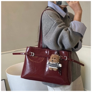 Dettaglio borsa tote in pelle verniciata rosso scuro con trama vintage e orsetto