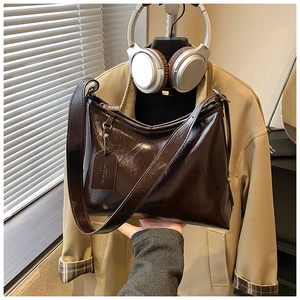 Detail of dark brown glossy patent leather bucket bag with wide strap and branded hardware