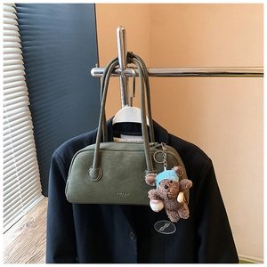 Gros plan du sac boston en daim vert foncé avec porte-clé ours et lettrage doré
