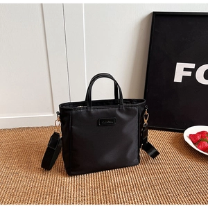 Close-up of minimalist black tote bag with gold hardware and wide nylon strap
