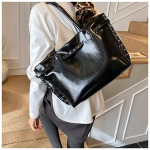 Close-up of black glossy patent leather tote bag featuring stylish silver metal rivets