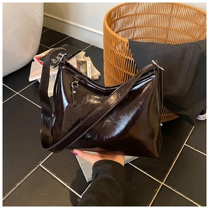 Detail of dark brown polished leather shoulder bag with wide strap and metallic hardware