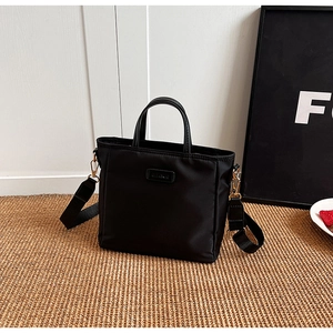 Detailed side view of black nylon tote bag with wide strap and leather handles