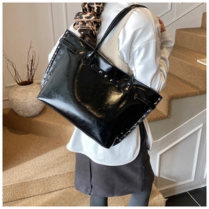 Detail of black patent leather tote bag with silver studs worn on shoulder in life scene