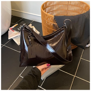 Detail of dark brown glossy patent leather texture on a minimalist commuter bucket bag