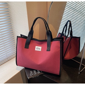 Détail d'un cabas en toile à carreaux rouges avec sangle noire et logo blanc
