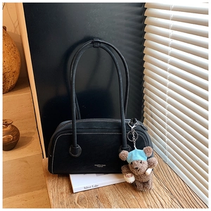 Détail du sac Boston noir en daim avec surpiqûres blanches et pendentif ours décoratif