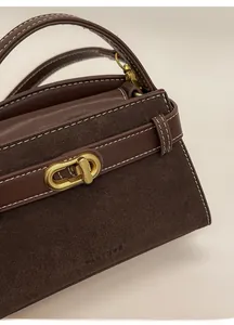 Detailed close-up of dark brown suede handbag with golden turn-lock and contrast stitching