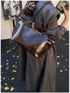 Detail of high-gloss tote bag with silver studs and autumn leaves in the background