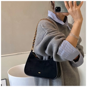 Detalle de bolso hobo de ante negro con cadena dorada y hebilla metálica minimalista