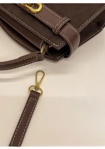 Detail view of dark brown retro crossbody bag with white stitching and gold hardware