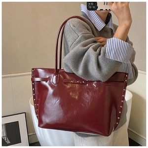 Detail of burgundy glossy leather tote bag with silver studs and decorative straps
